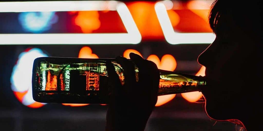 female drinking beer in front of neon lights